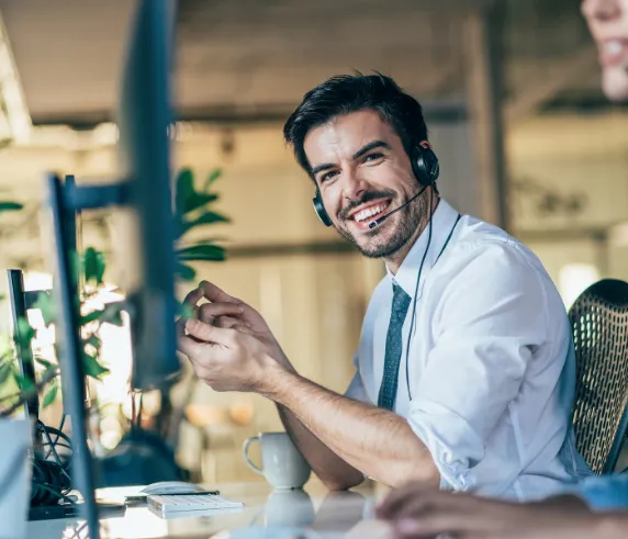 Homem sorridente usando um fone de ouvido enquanto trabalha em um computador